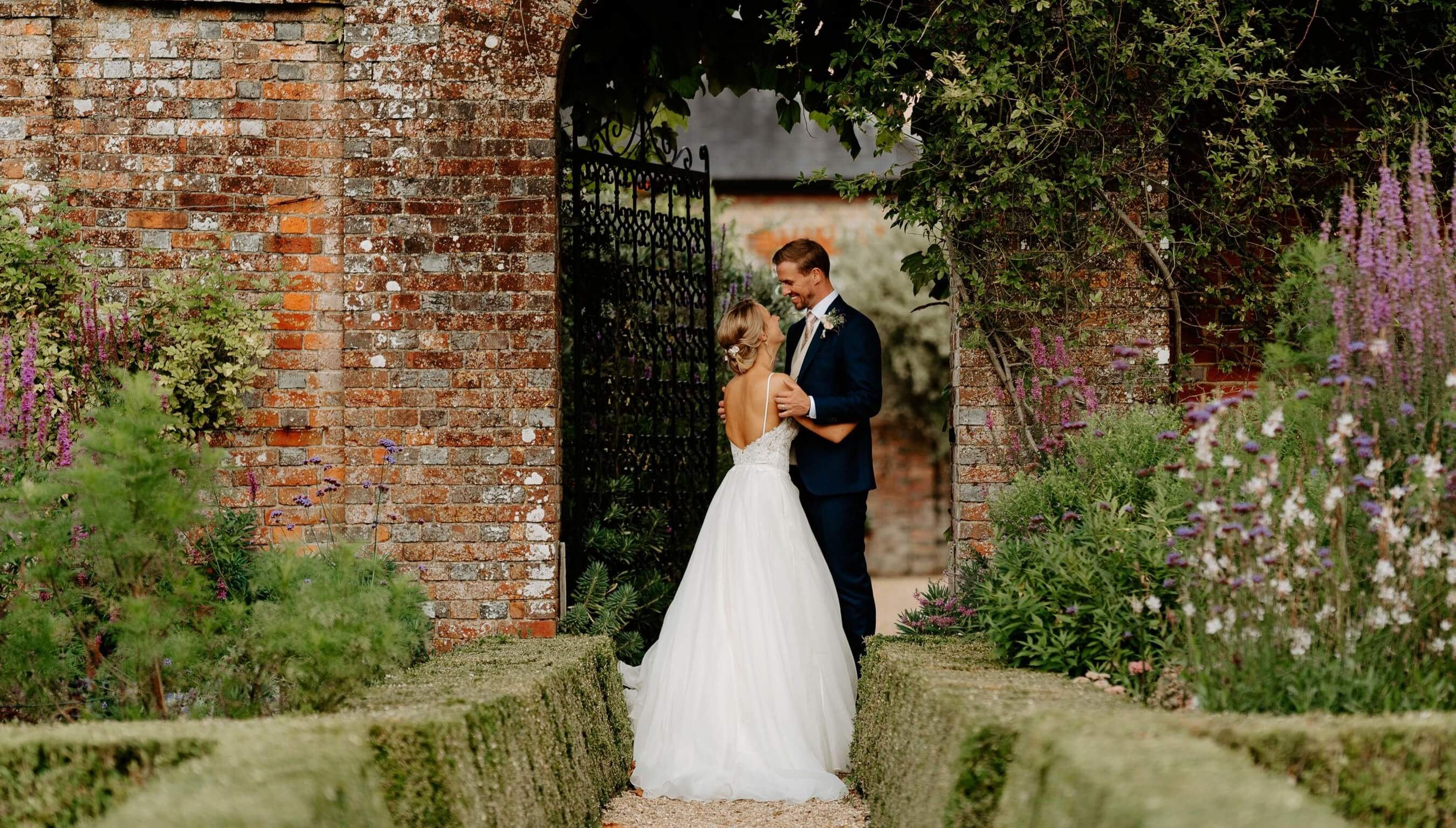 Bride and groom portrait in walled gardens at Bignor Park West Sussex with brick archway and romantic outdoor wedding setting