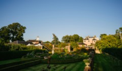Wide view of Bignor Park’s formal gardens at golden hour, with sculpted hedging, flowering borders and the house beyond in the West Sussex countryside