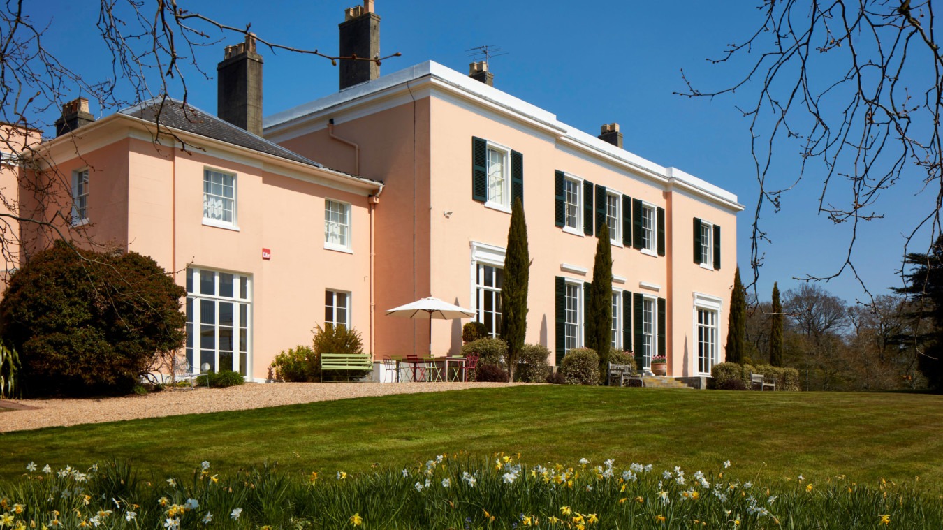 The elegant Georgian façade of Bignor Park in West Sussex, with soft pink stucco, tall sash windows viewed from the South Lawn