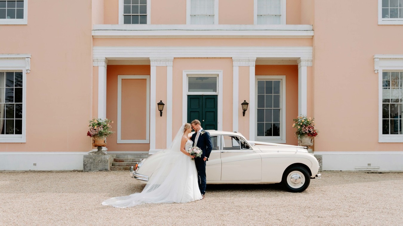 Wedding couple in front of Bignor Park country house in West Sussex with vintage car