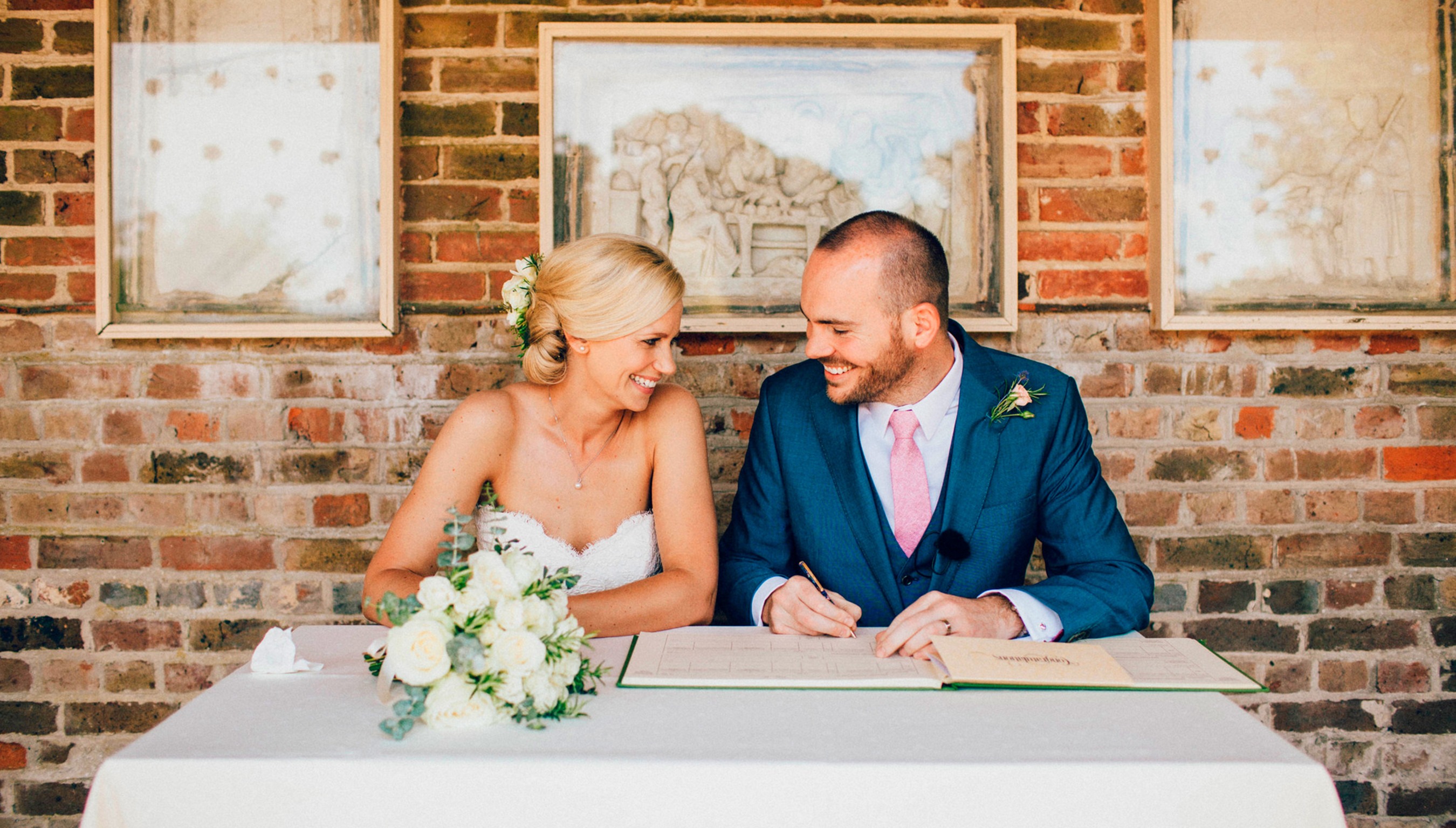 Outdoor wedding, Signing the register together, sharing a quiet, joyful moment just after saying “I do” at Bignor Park's Greek Loggia