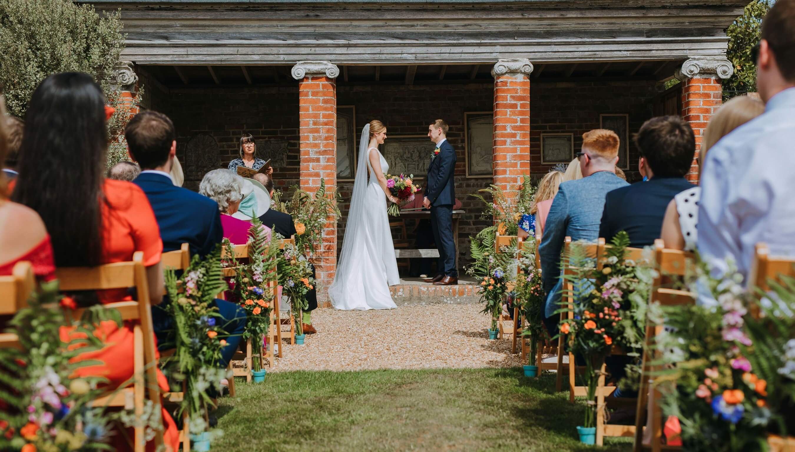 Outdoor wedding ceremony at the Greek Loggia at Bignor Park Sussex with guests seated outdoors
