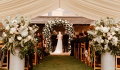 Wedding ceremony inside marquee at Bignor Park in West Sussex with floral arch and aisle seating