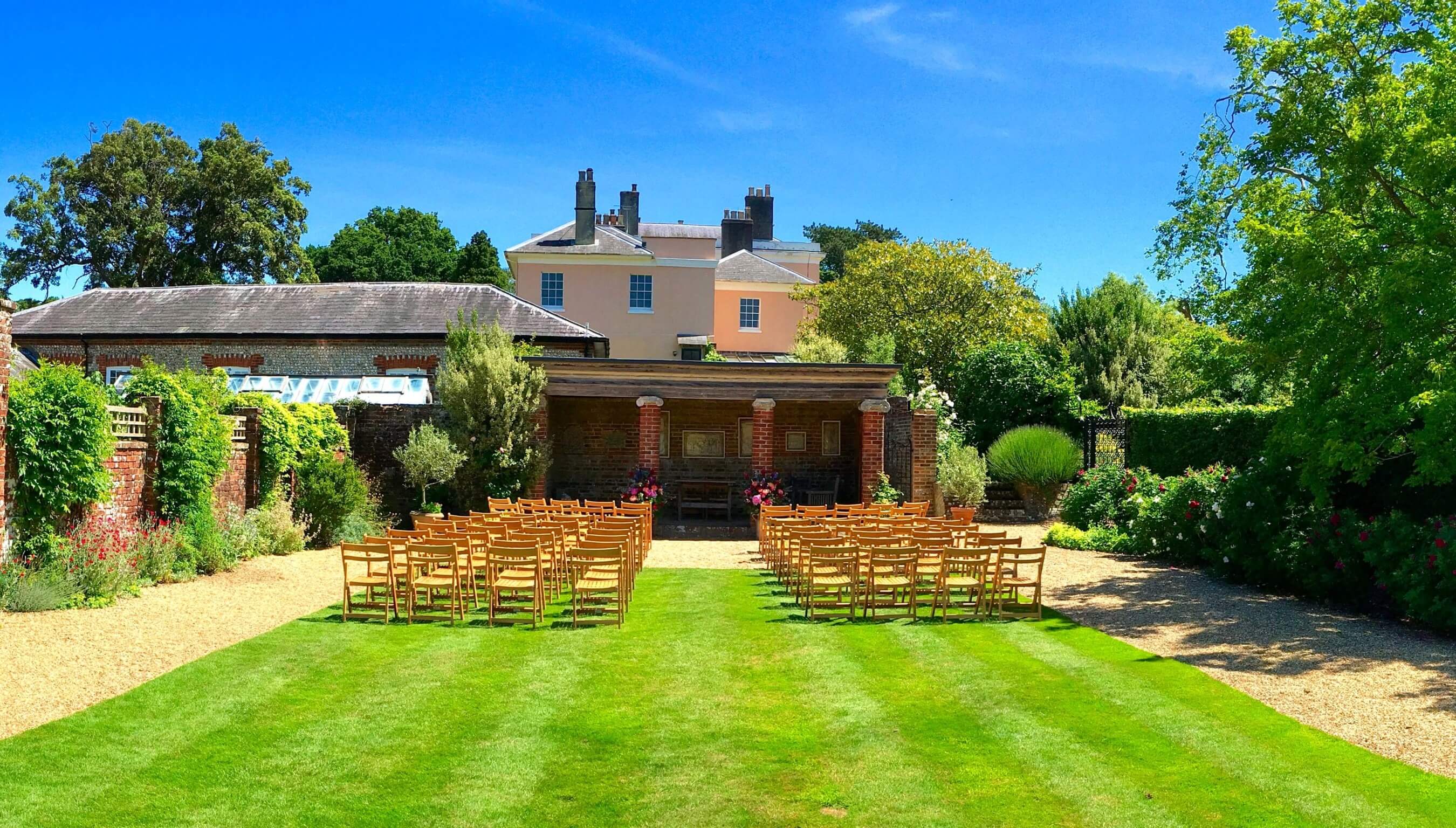 Outdoor wedding ceremony setup at the Greek Loggia at Bignor Park in West Sussex with garden seating