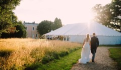 Bride and groom walking through Bignor Park grounds in West Sussex towards wedding marquee on the Croquet lawn at sunset