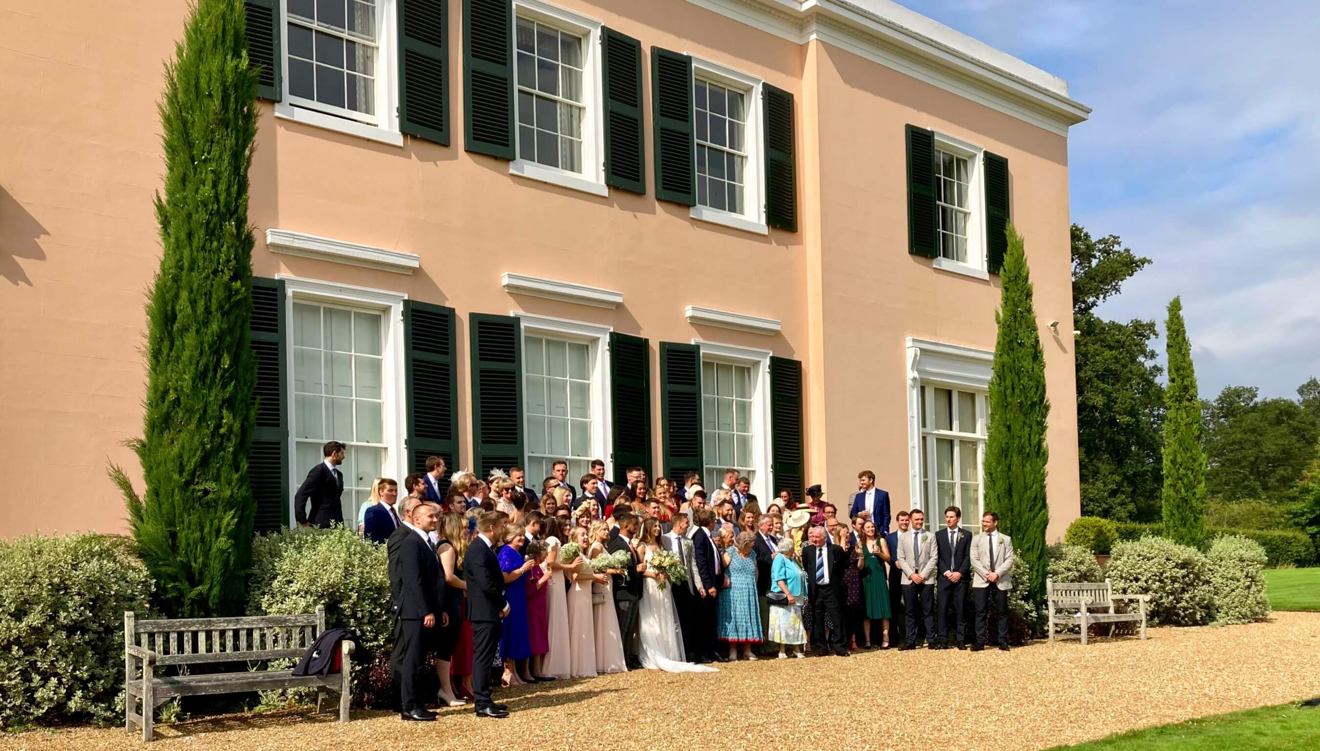 Wedding guests gathered for a group photo outside Bignor Park house in West Sussex during a countryside wedding celebration