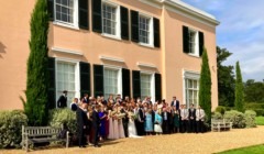 Large wedding group photo outside Bignor Park country house with guests gathered in front of peach facade and green shutters