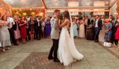 Bride and groom sharing their first dance in the Stables Quadrangle at Bignor Park with guests gathered around under festoon lighting