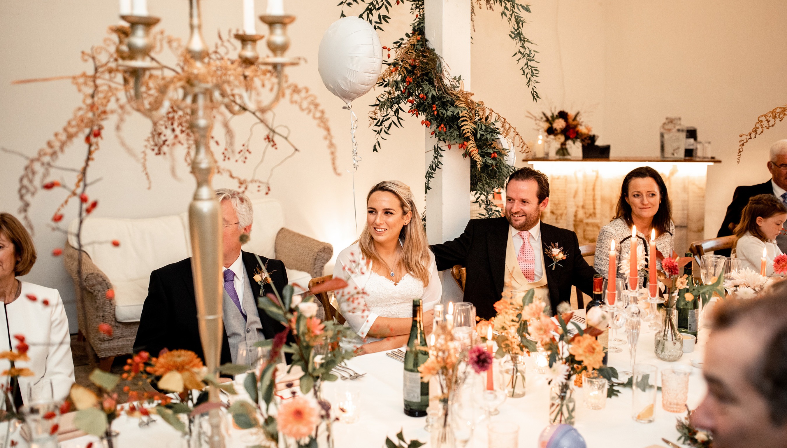 Bride and groom seated at wedding breakfast in The Stables at Bignor Park in West Sussex with floral table decorations and candlelight
