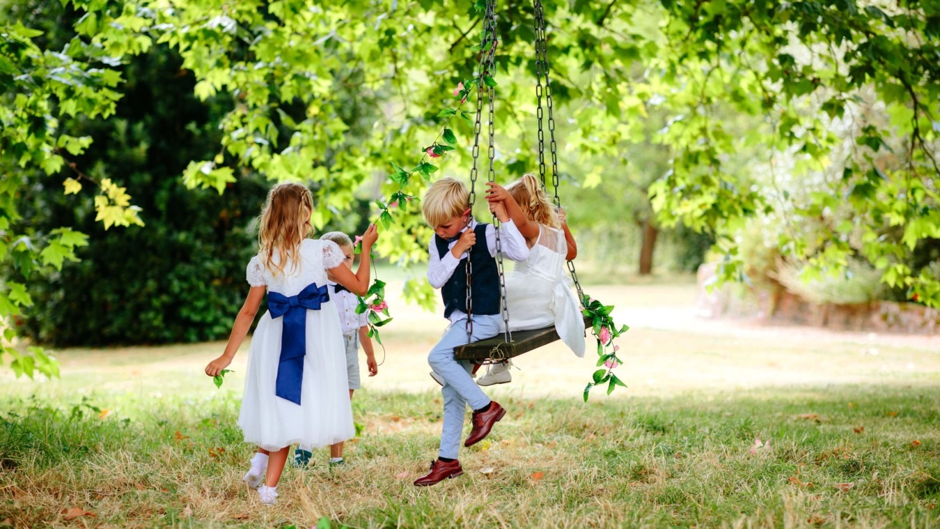 Children playing on a swing under trees at Bignor Park during a summer wedding