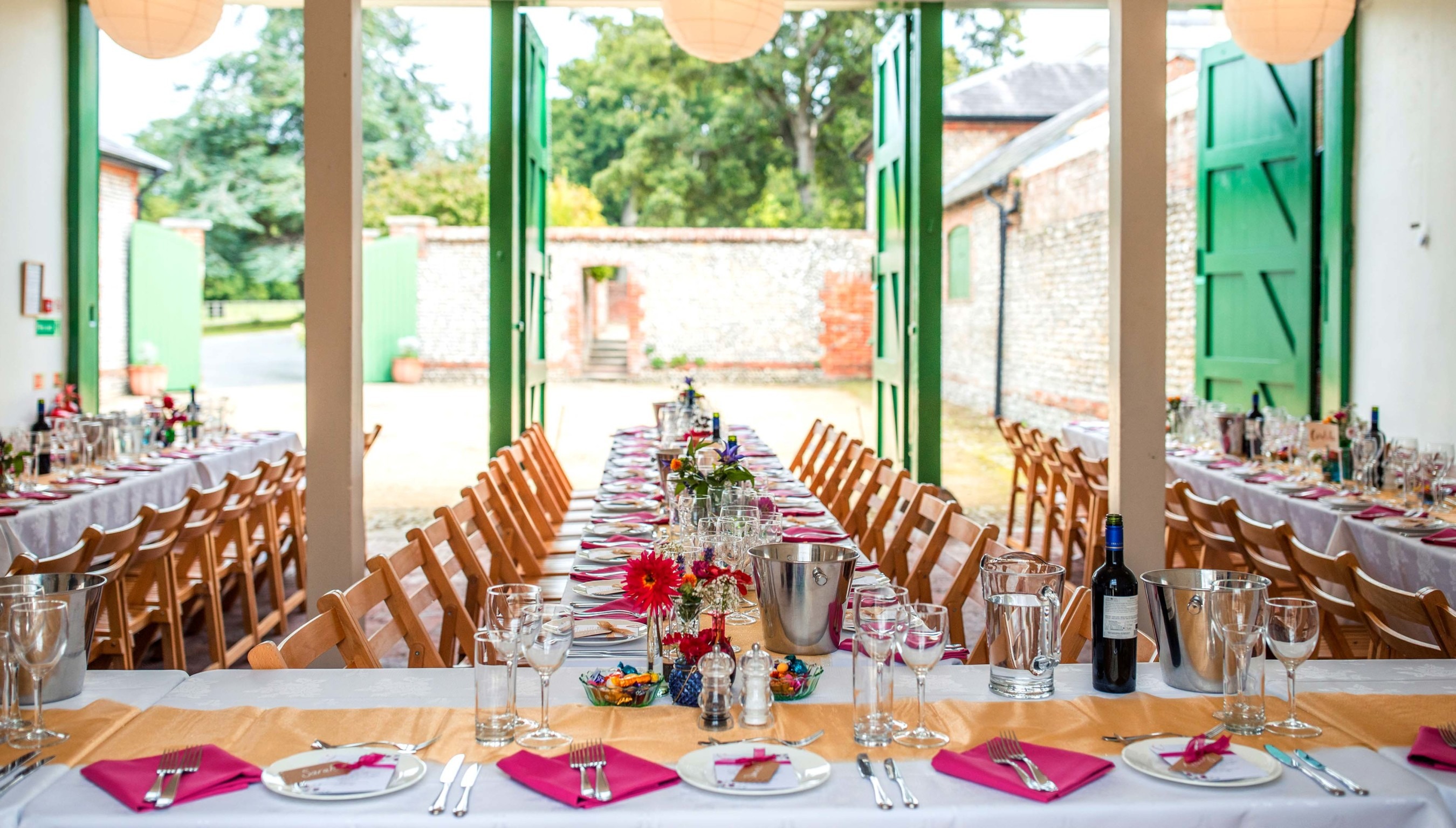 A set up for a wedding breakfast with the green stables doors open and looking out to the quadrangle at Bignor Park