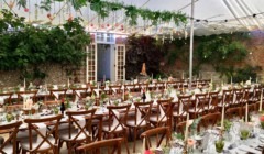 Wedding reception tables set in courtyard marquee at Bignor Park West Sussex with festoon lighting and floral décor