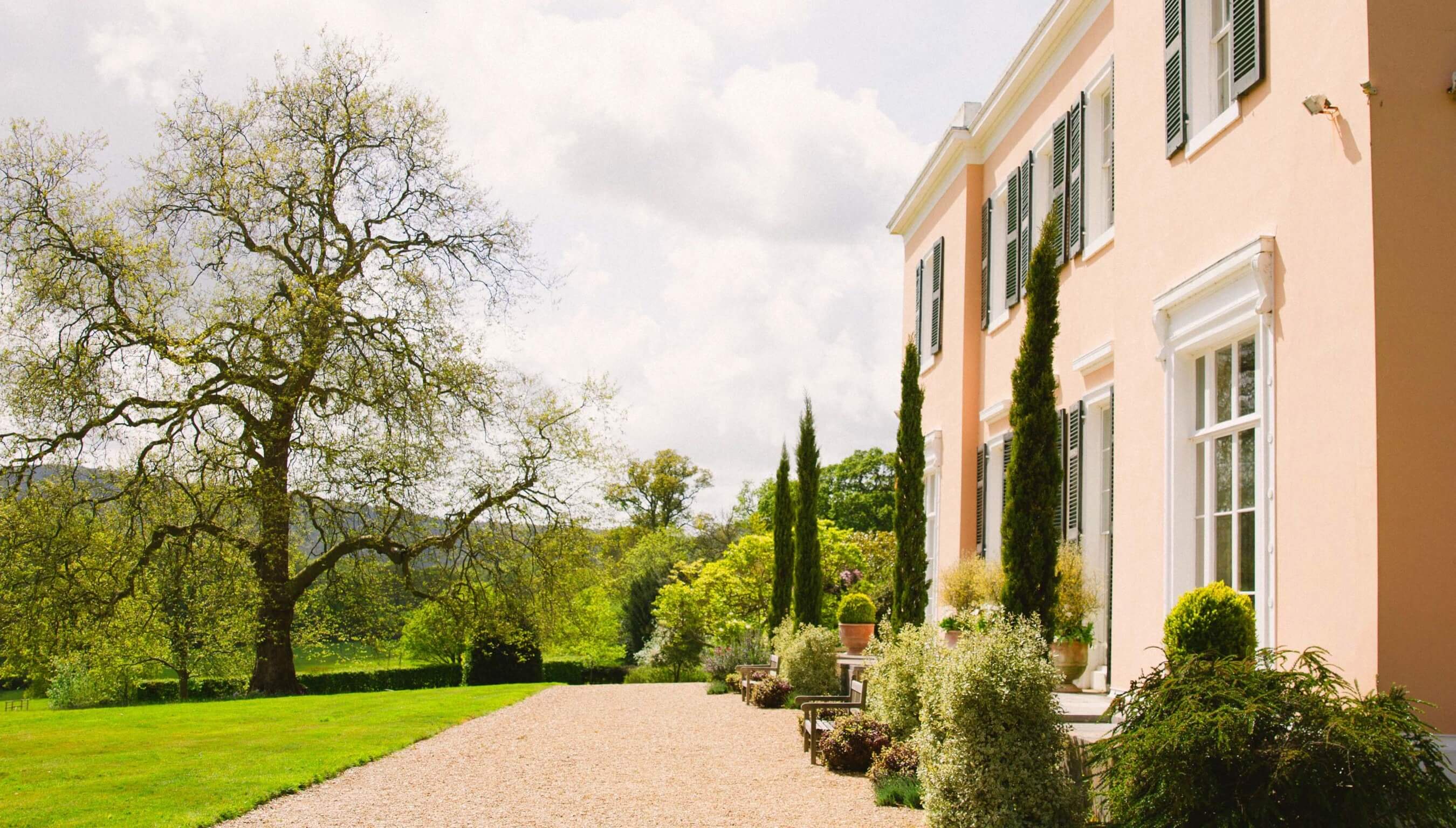 Outdoor wedding venue Bignor Park Georgian country house exterior in West Sussex with landscaped gardens, gravel terrace and mature trees in soft sunlight
