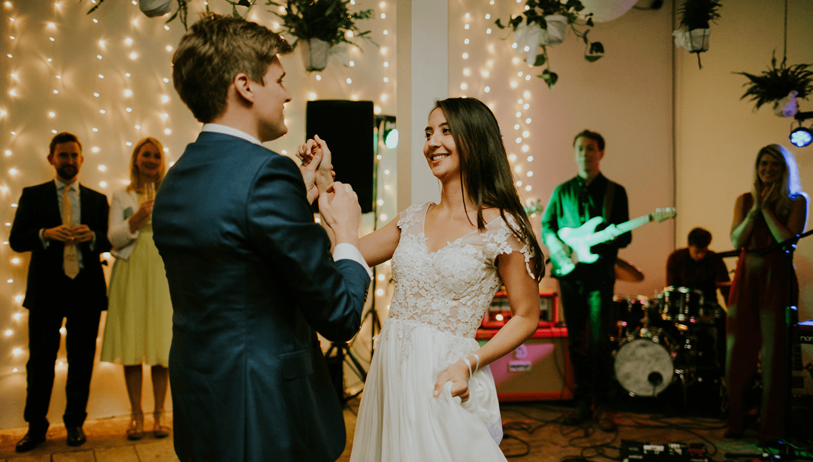Bride and groom sharing their first dance at a Bignor Park wedding reception, with live band and fairy lights creating a warm, intimate atmosphere in The Stables