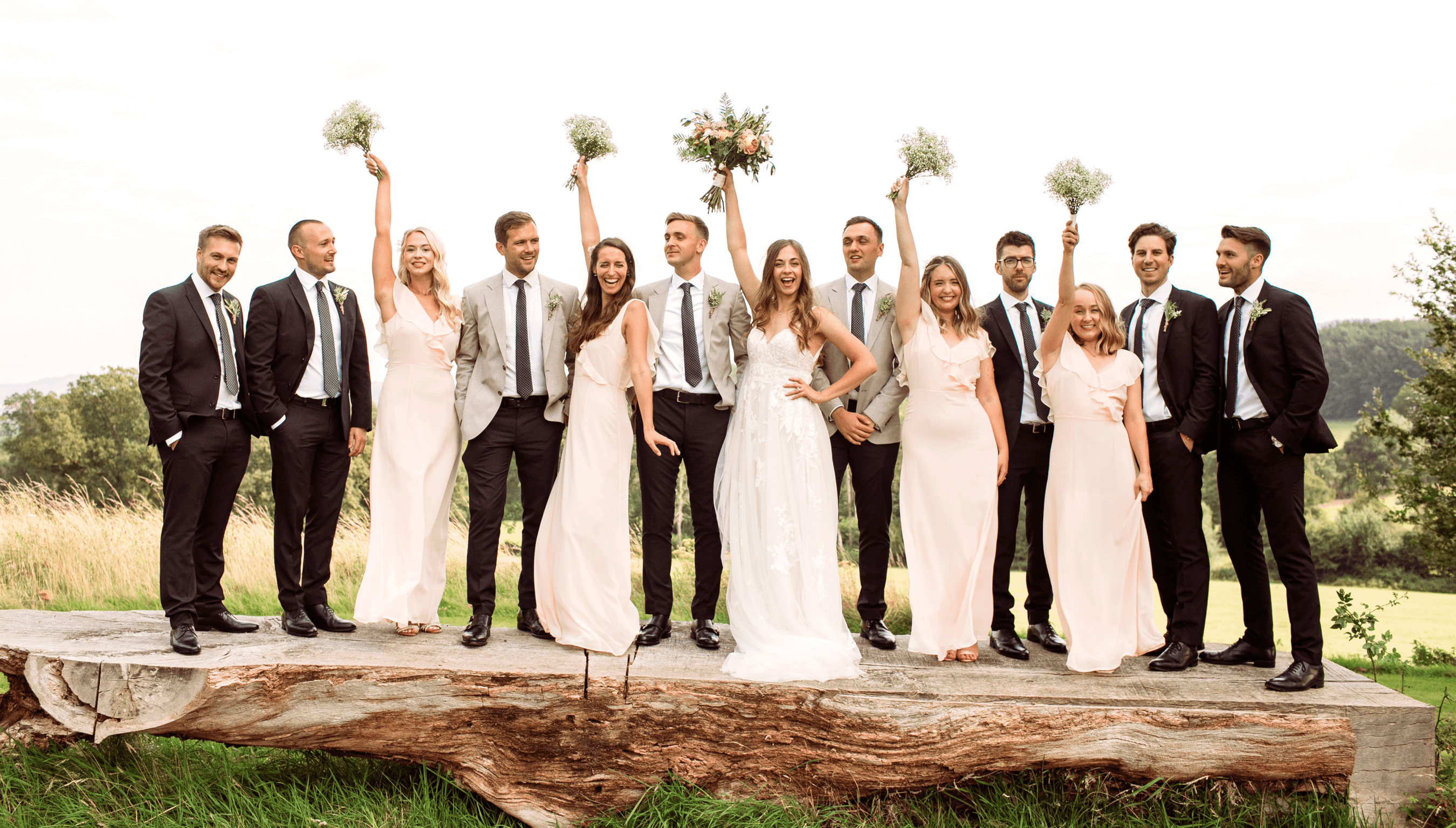 Best men and Bridesmaids raising bouquets standing on the tree table on the South lawn of Bignor Park during an outdoor wedding