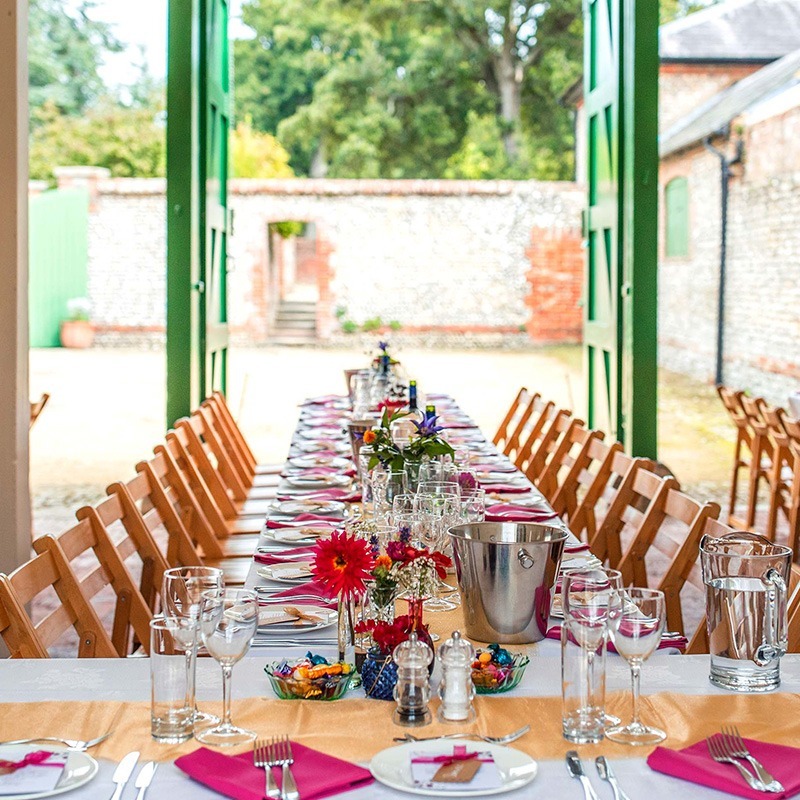 Wedding breakfast setup inside Bignor Park Stables with long banquet tables, floral centrepieces and open green barn doors